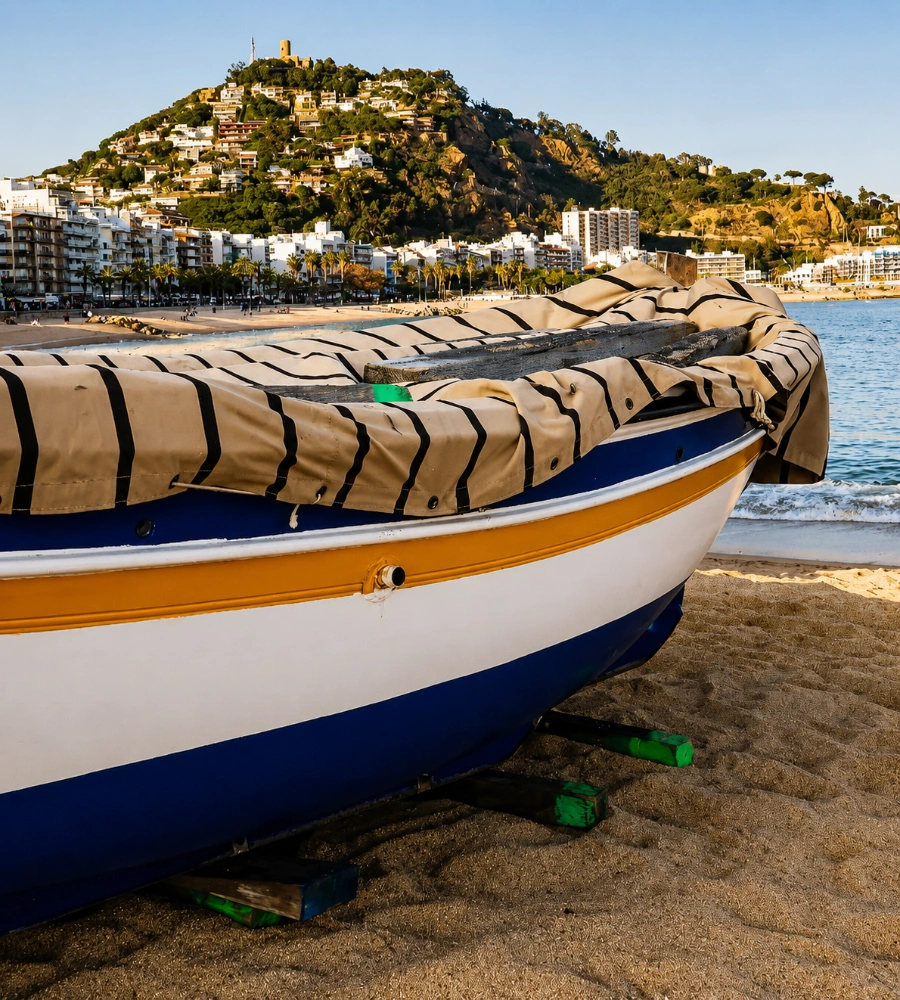 Barca blanca y azul en la playa, con cerro y edificios al fondo