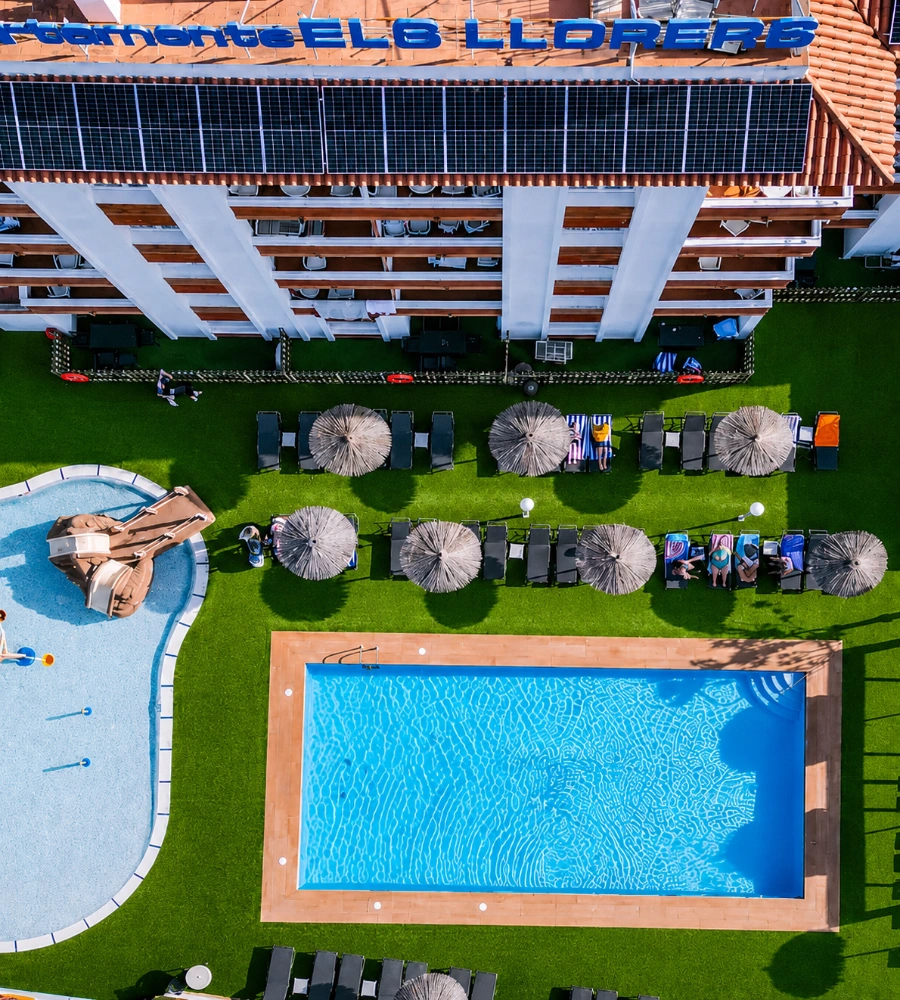 Piscina y terraza con c&eacute;sped, tumbonas y sombrillas junto a la fachada &ldquo;ELB LLOREI&rdquo;