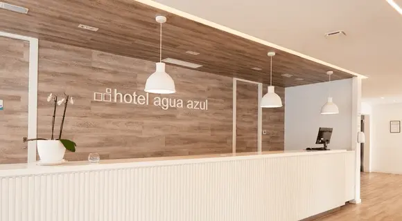 Recepci&oacute;n del hotel Agua Azul con mostrador blanco y luces colgantes.