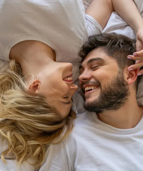 Pareja abrazada en la cama, ri&eacute;ndose y bes&aacute;ndose con ternura