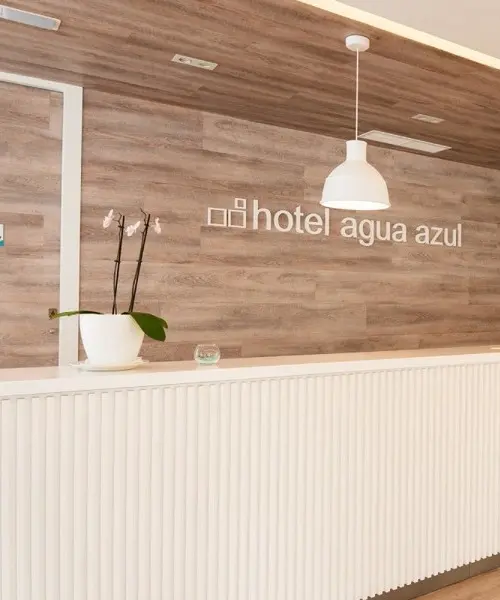 Recepci&oacute;n de hotel con pared de madera y l&aacute;mpara colgante.