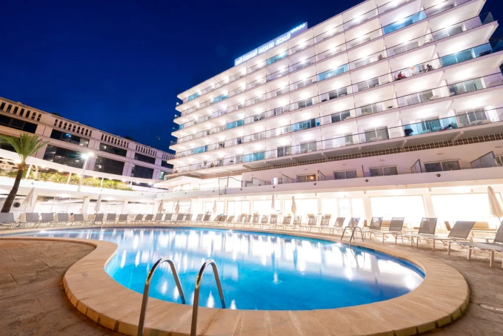 Piscina y hotel iluminado de noche con cielo azul
