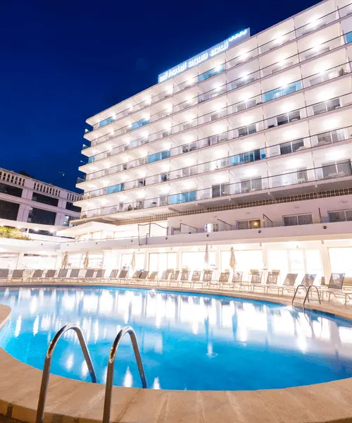 Piscina azul y hotel moderno iluminado de noche con fachada blanca