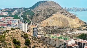 Vista aérea de edificios costeros y un cerro rocoso junto al mar.