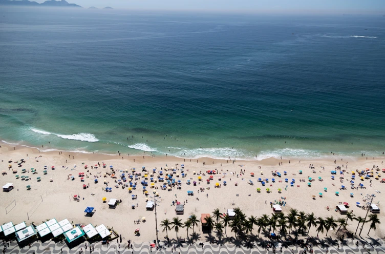 Playa tropical con mucha gente, palmeras y olas frente al mar.