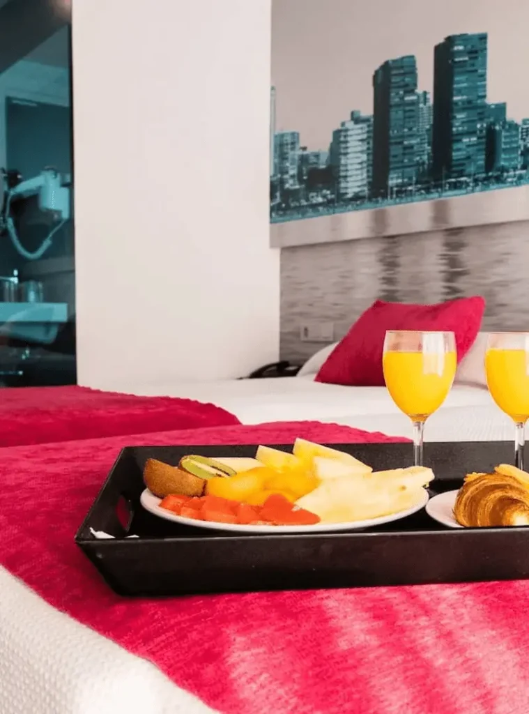 Mesa con desayuno: bandeja, frutas, tostadas y dos copas de jugo en cama roja