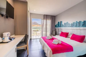 Habitaci&oacute;n de hotel moderna con cama, cortinas y vista a la ciudad y mar