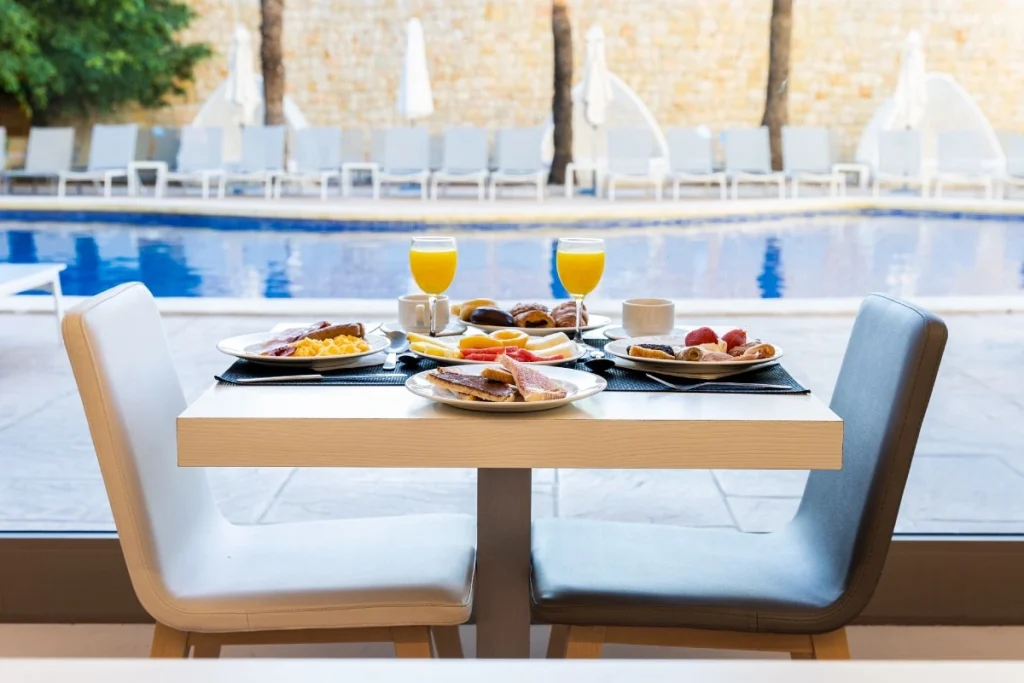 Mesa con desayuno junto a la piscina, con platos de frutas y jugo