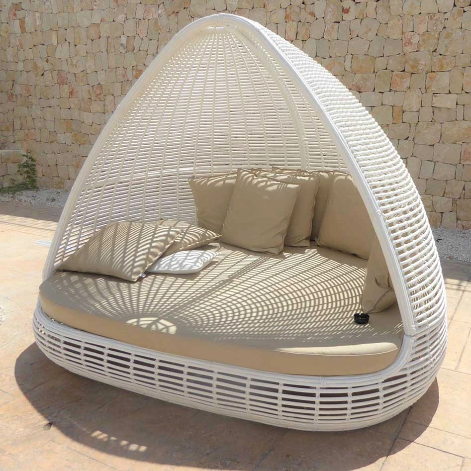 Sill&oacute;n de mimbre blanco con cojines beige, junto a una pared de piedra.