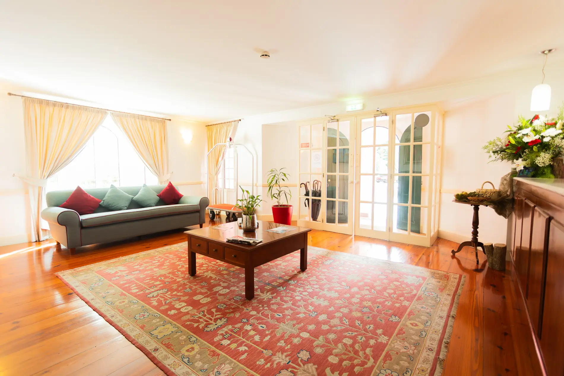 Sala de estar iluminada com sof&aacute;, mesa de centro e tapete vermelho estampado.