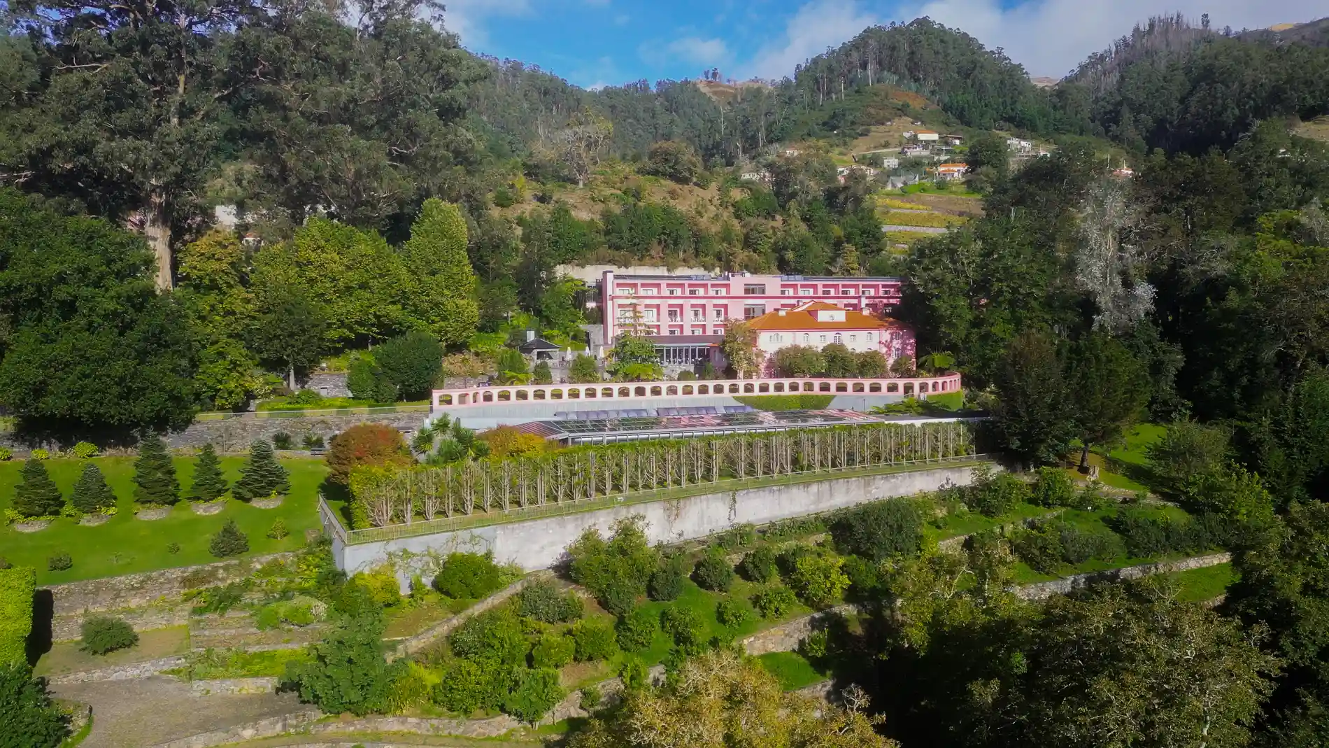 Edif&iacute;cio rosa rodeado por vegeta&ccedil;&atilde;o luxuriante e colinas verdejantes.