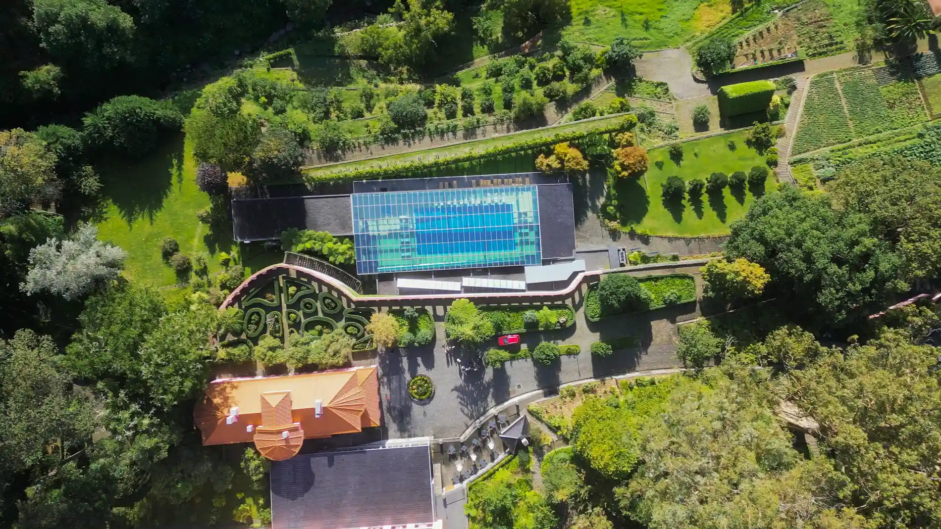 Vista a&eacute;rea de jardim com piscina e constru&ccedil;&atilde;o em meio &agrave; vegeta&ccedil;&atilde;o.