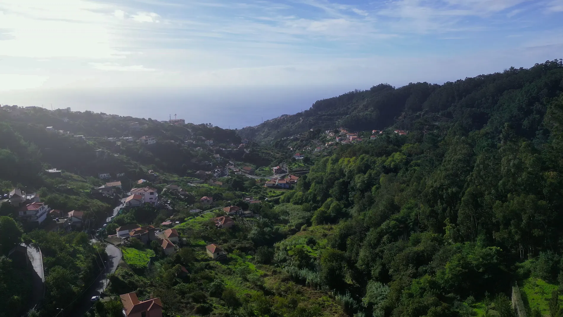 Vista a&eacute;rea de um vale verde com casas e colinas ao fundo.