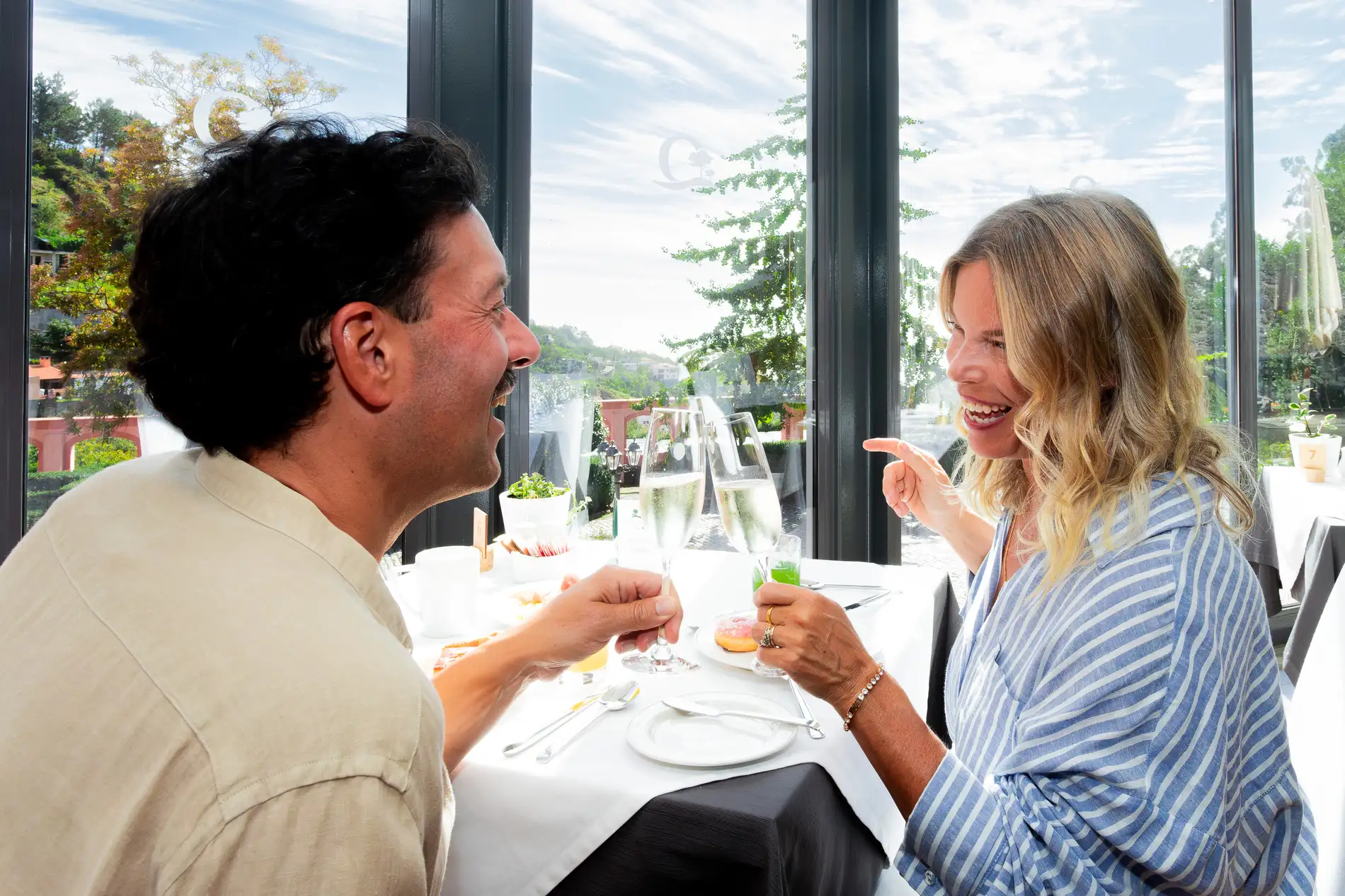 Casal sorrindo em uma refei&ccedil;&atilde;o, brindando em ambiente iluminado.