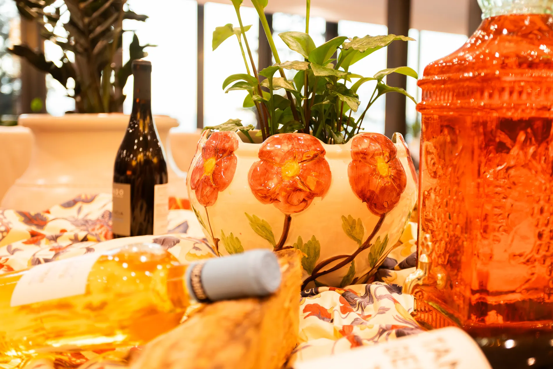 Vaso de cer&acirc;mica floral com garrafas de vinho ao redor.