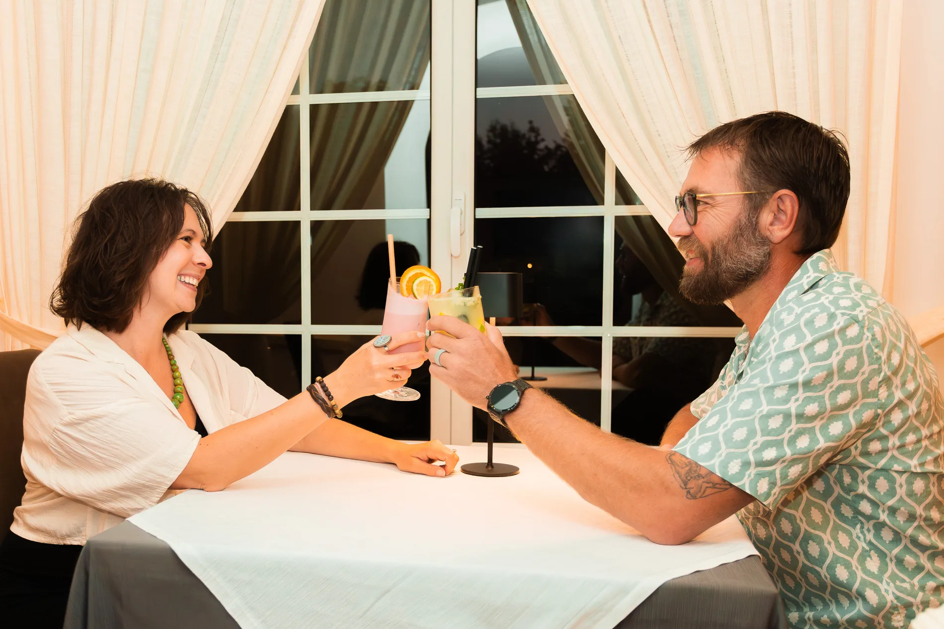 Casal brindando com coquet&eacute;is em uma mesa de jantar.