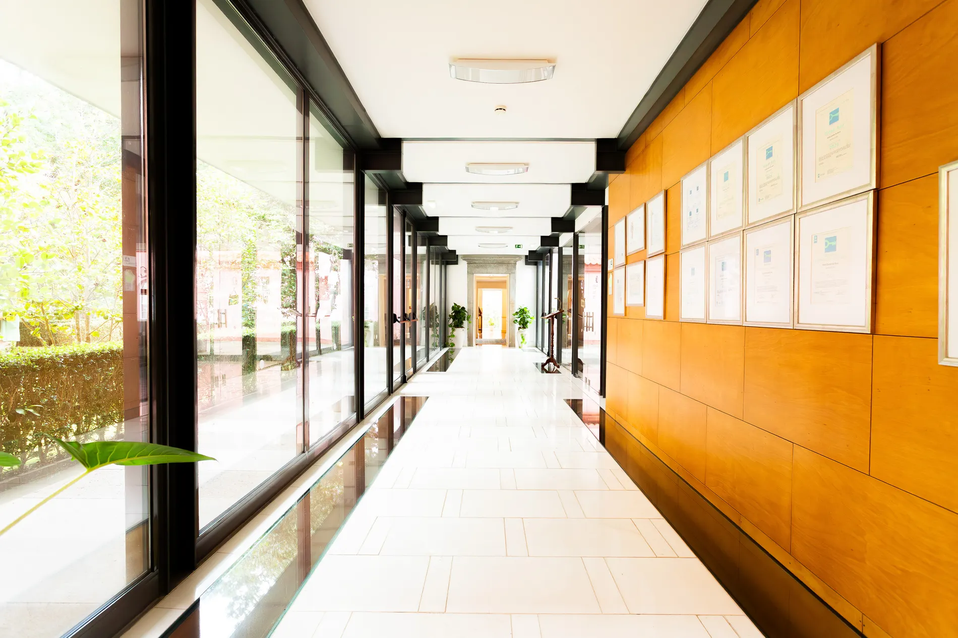 Corredor com piso claro, janelas amplas e quadros na parede de madeira.
