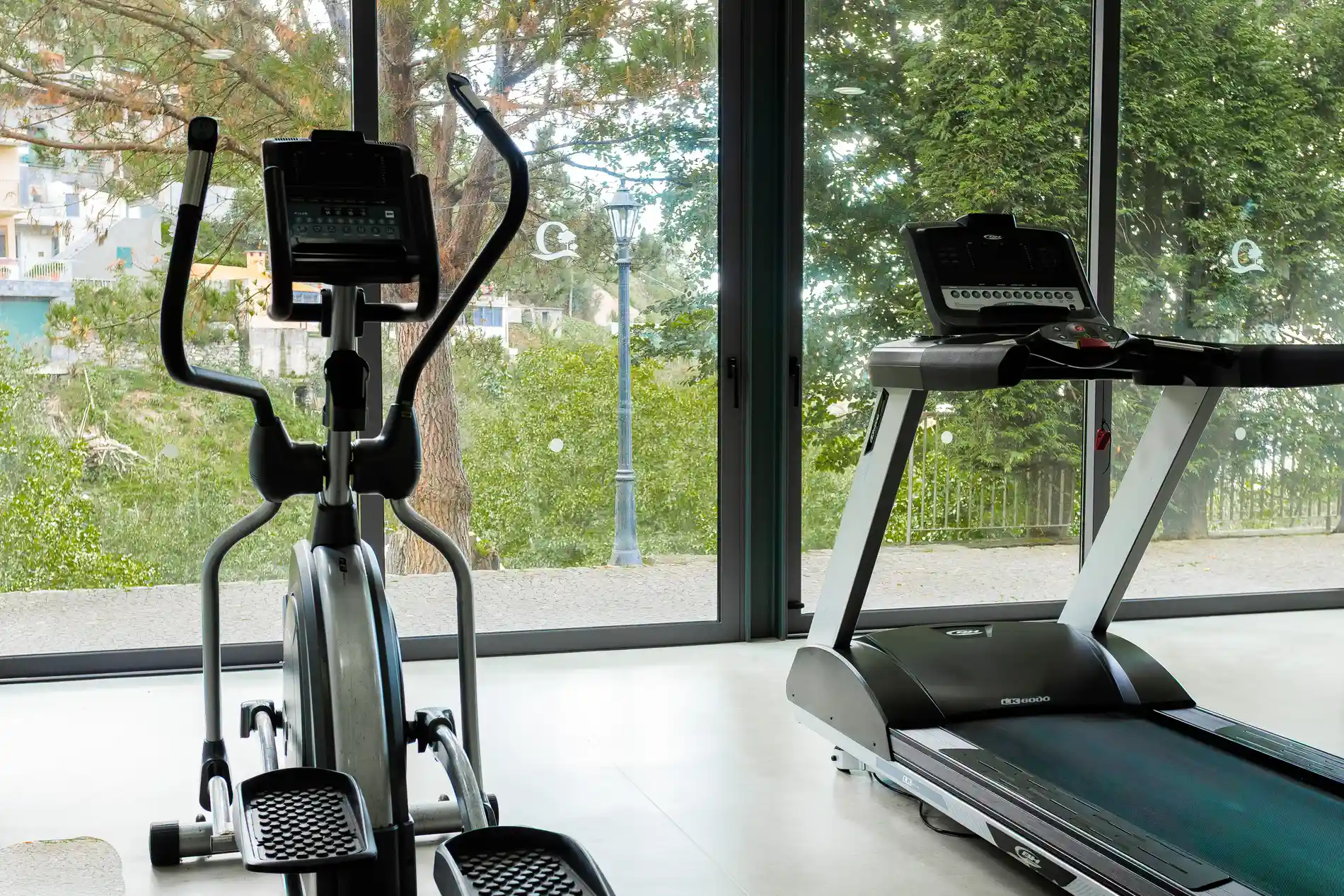 M&aacute;quina el&iacute;ptica e esteira em academia com vista para &aacute;rvores.