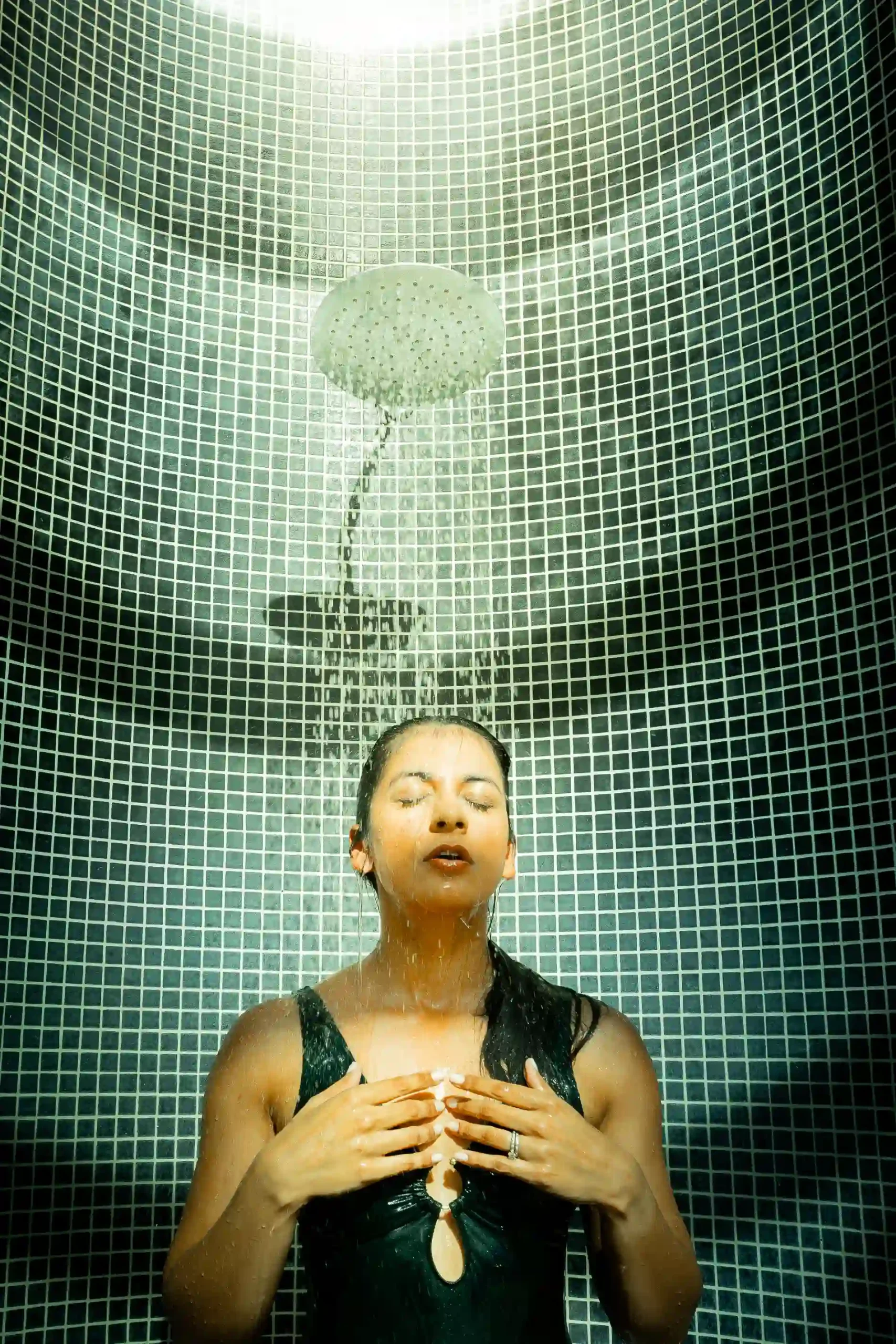 Pessoa tomando banho sob um chuveiro com azulejos brancos ao fundo.