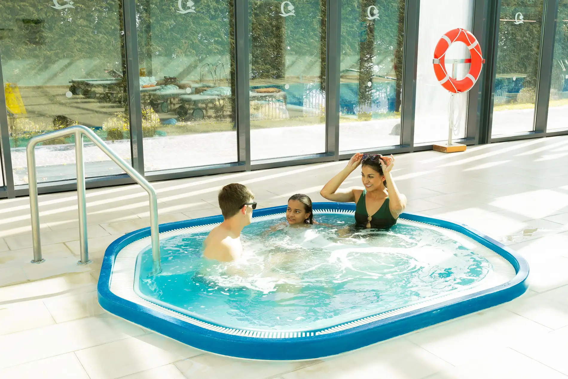 Tr&ecirc;s pessoas relaxando em uma banheira de hidromassagem interna iluminada.