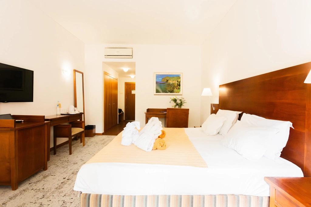 Quarto de hotel com cama, TV e m&oacute;veis de madeira.