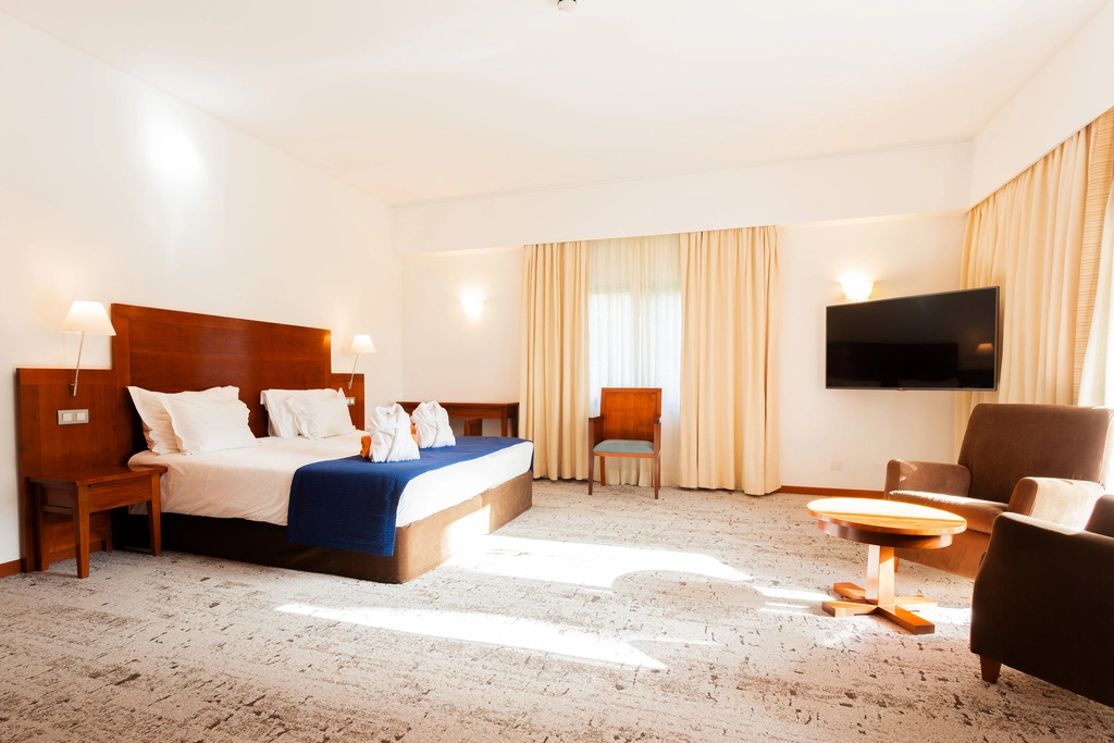 Quarto de hotel elegante com cama, TV e poltronas.