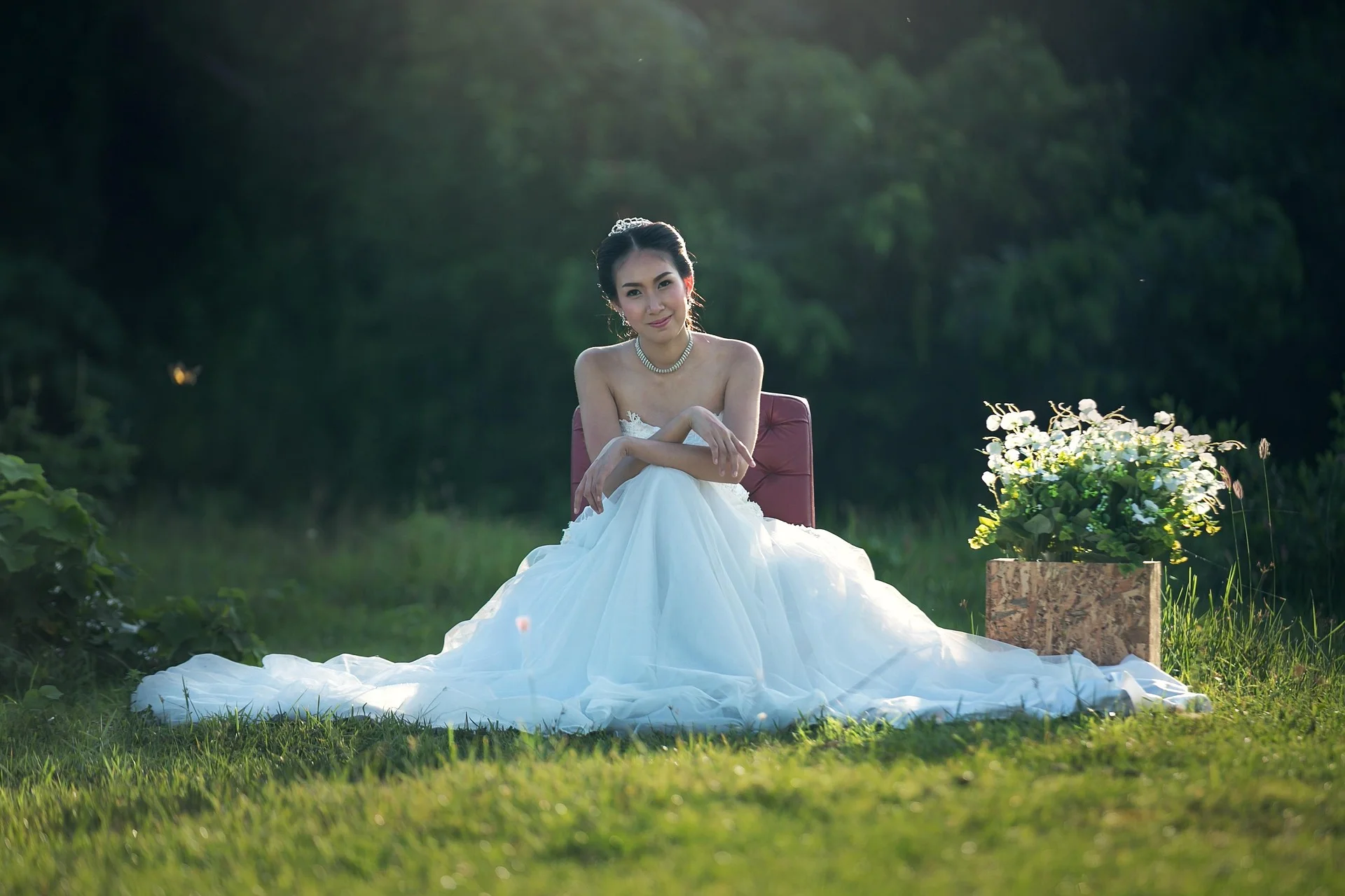 Noiva sentada em cadeira no campo, vestido branco e flores ao lado.