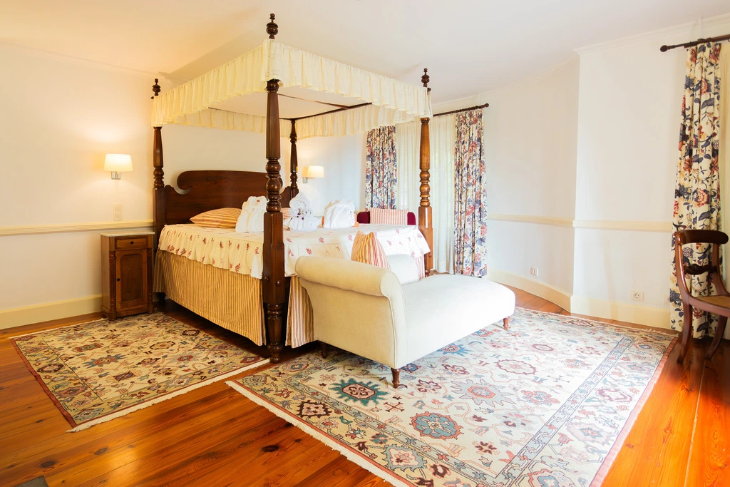 Quarto elegante com cama dossel, sof&aacute; e tapetes decorativos.