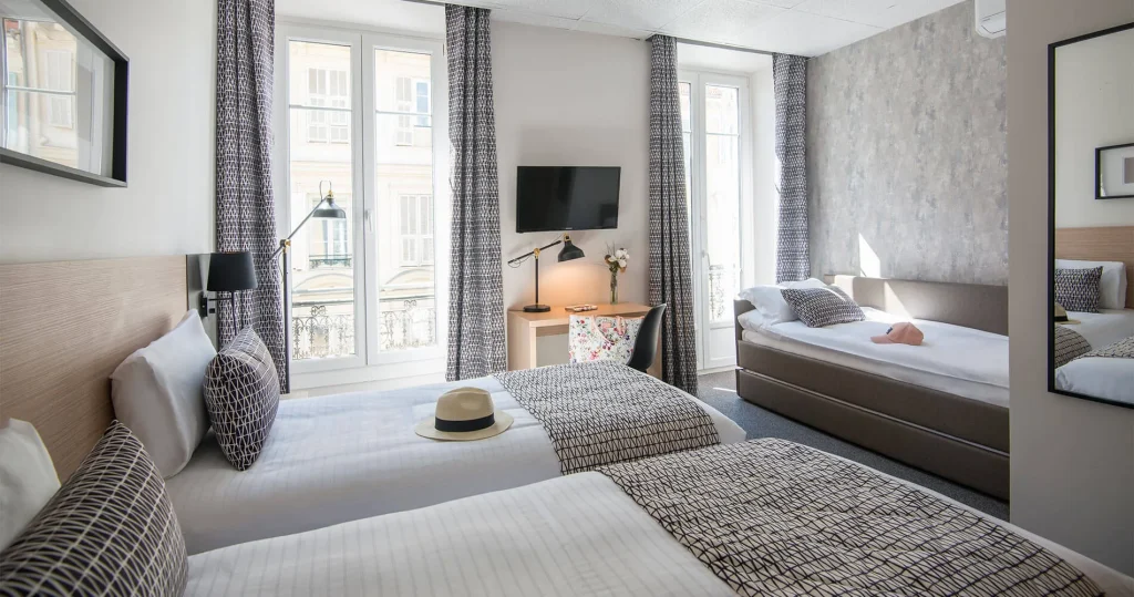Habitaci&oacute;n moderna con dos camas, sof&aacute; y ventanas grandes.