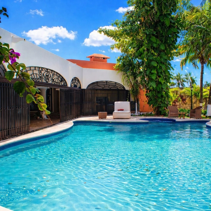 Piscina al aire libre rodeada de palmeras y una casa blanca.