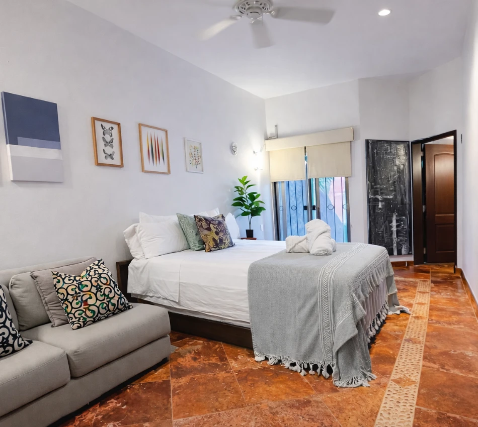 Habitaci&oacute;n moderna con cama, sof&aacute;, arte en la pared y planta junto a la ventana.