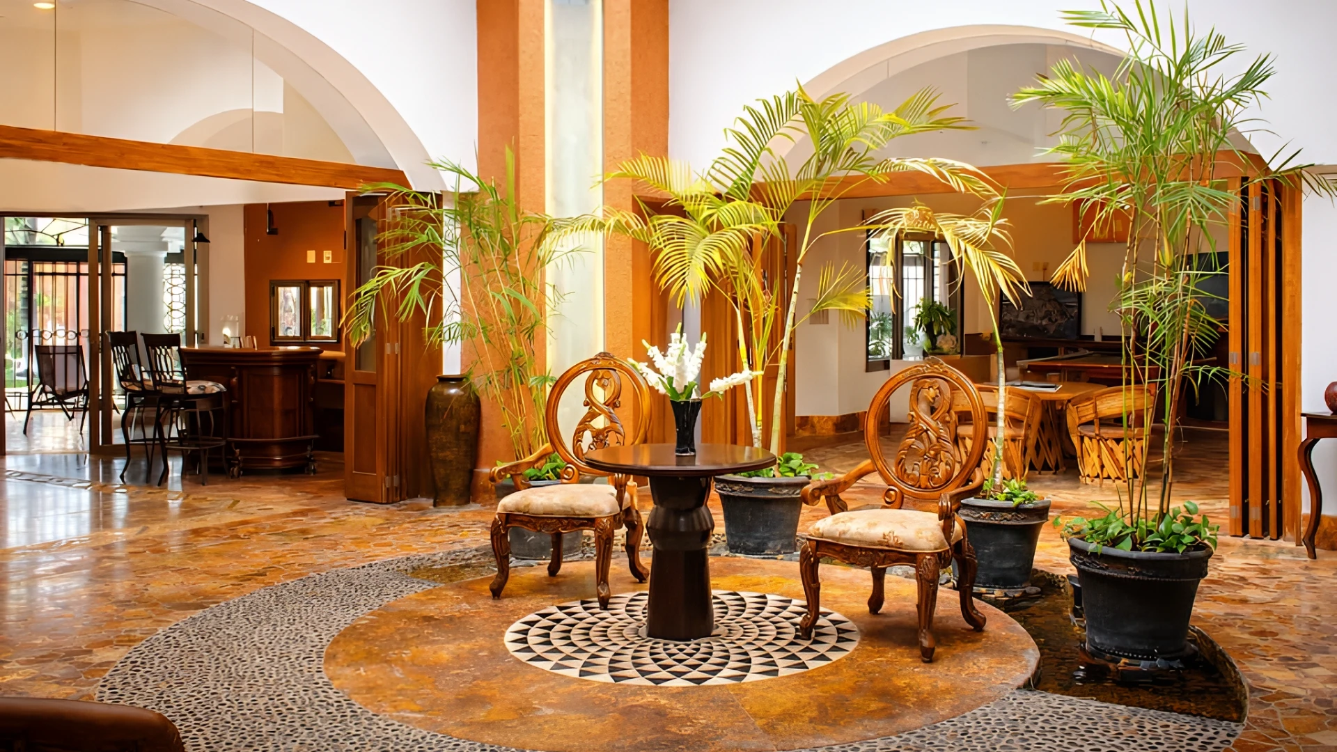 Sal&oacute;n elegante con sillas talladas, plantas y una mesa central.