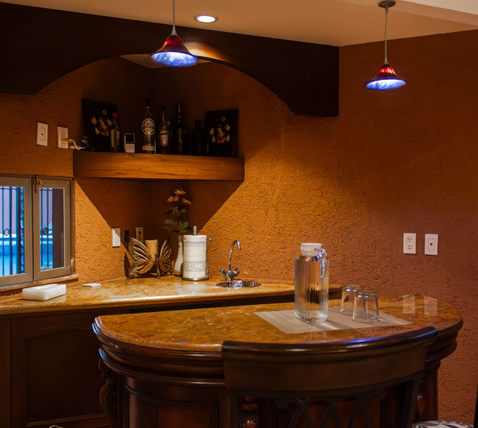 Bar con estanter&iacute;a de licores, mesa de m&aacute;rmol, silla y jarras de vidrio.
