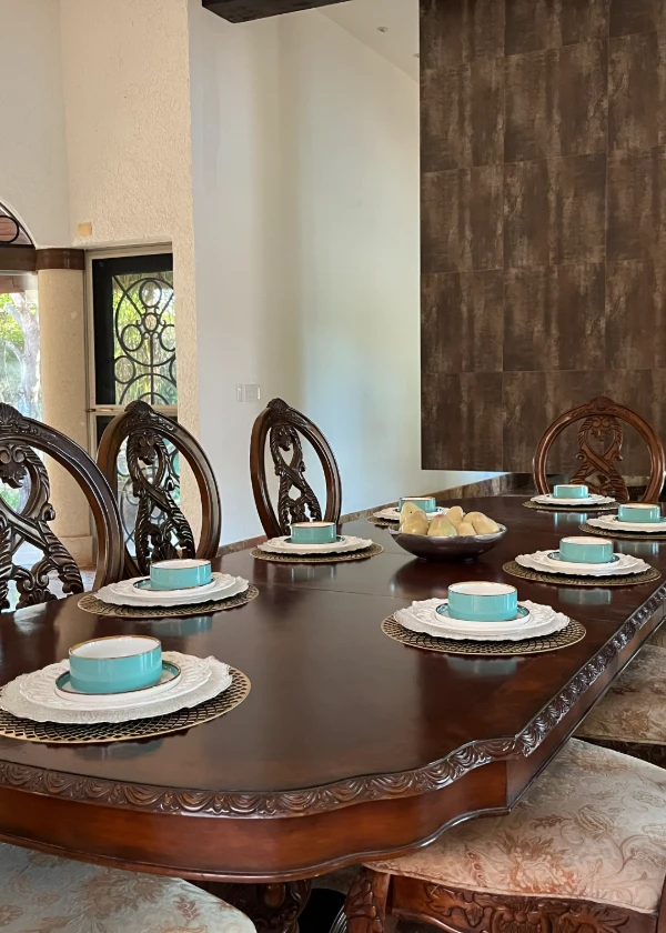 Mesa elegante con vajilla turquesa y silla de madera tallada.