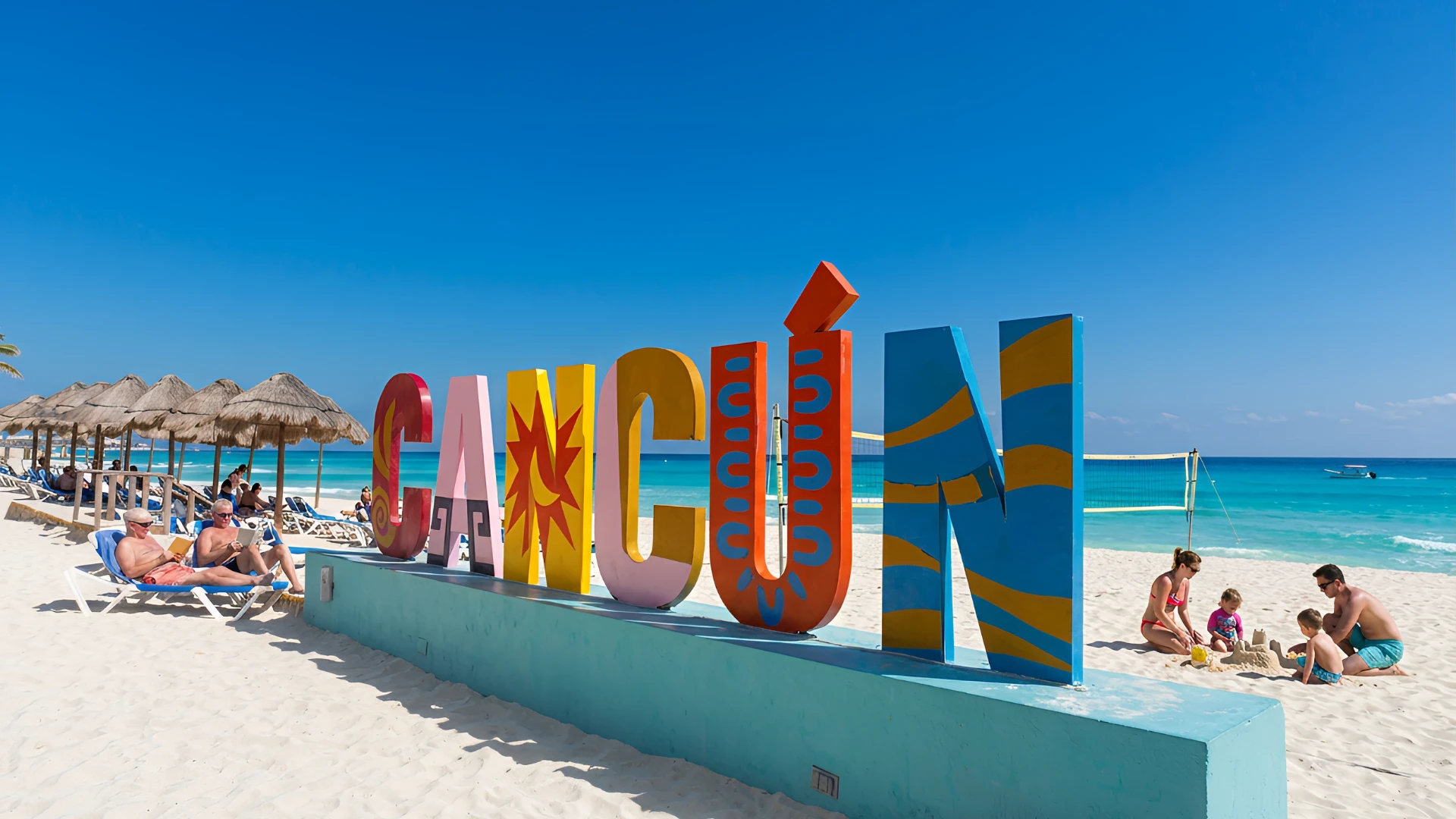 Playa con letrero de Canc&uacute;n, sombrillas, turistas y mar azul.