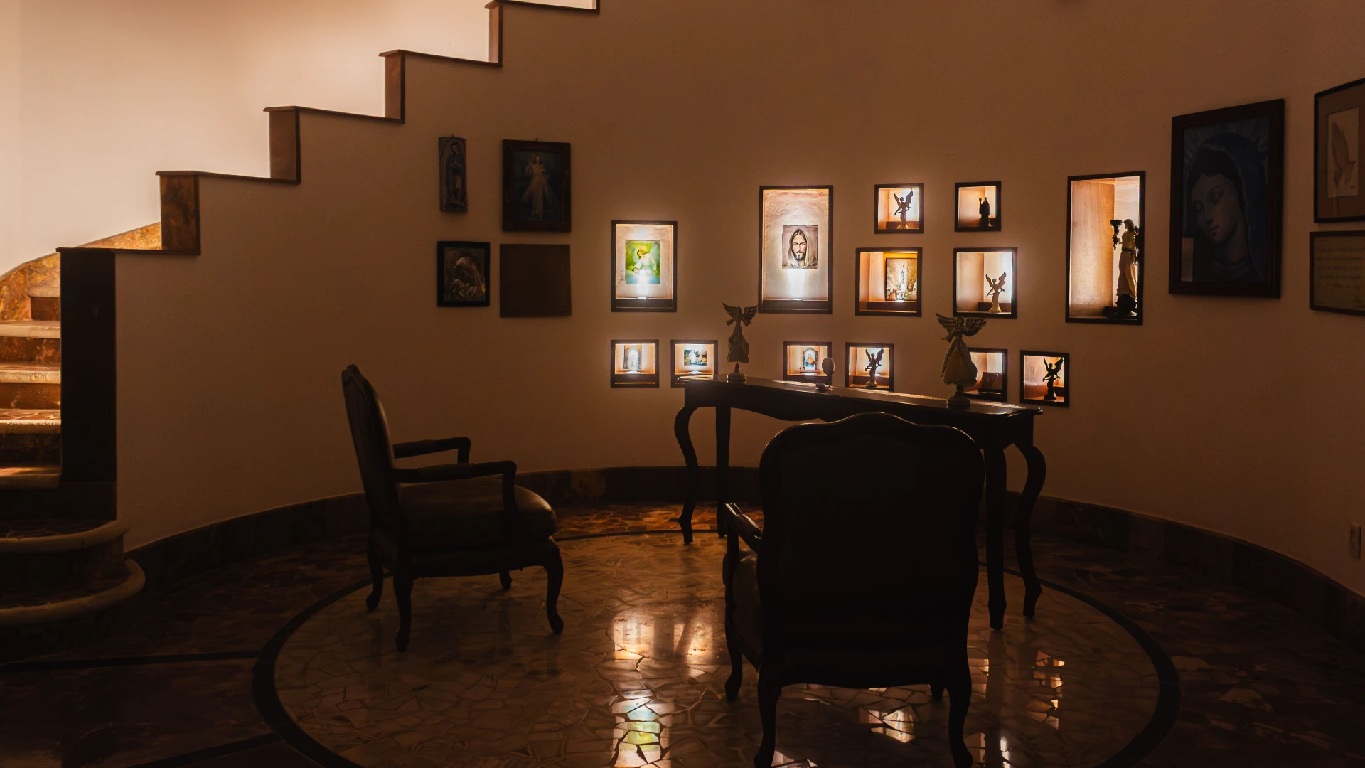 Sala con sillas, cuadros iluminados y escaleras a la izquierda.