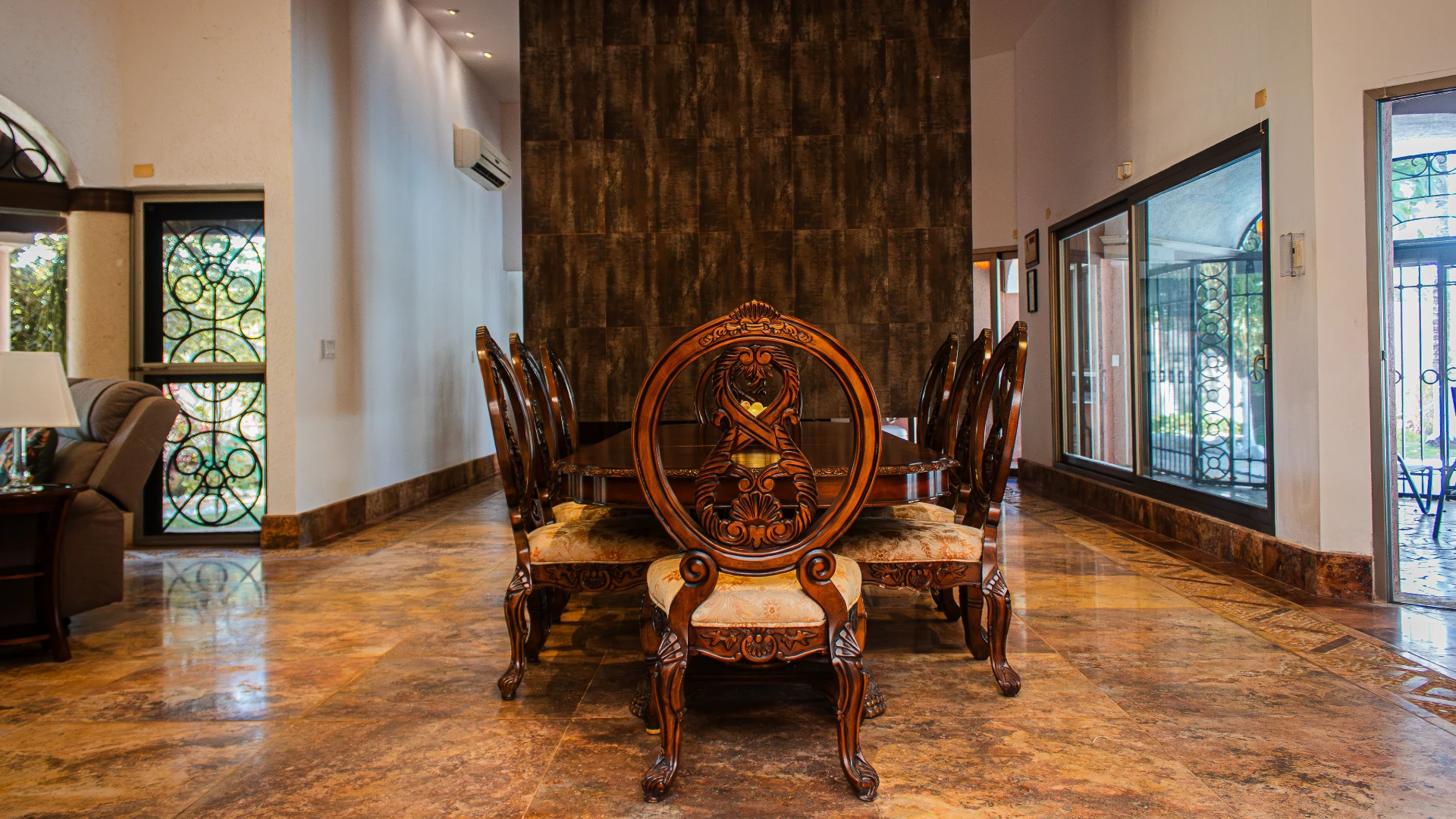 Comedor elegante con sillas talladas y mesa de madera en un sal&oacute;n amplio.