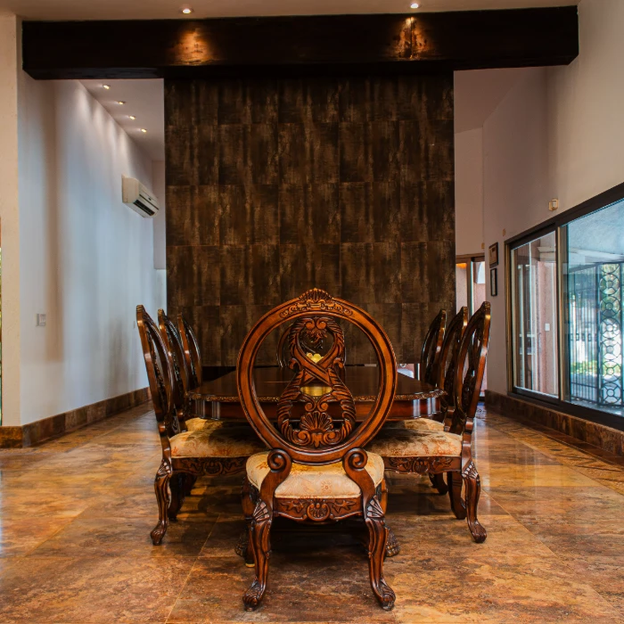 Comedor elegante con mesa y sillas de madera tallada y pared oscura de fondo.