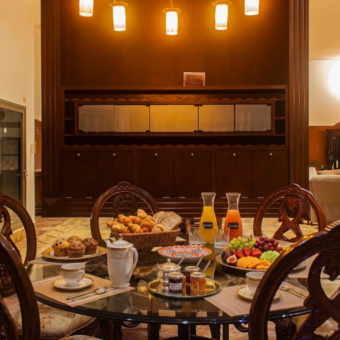 Mesa con desayuno, frutas, boller&iacute;a, jugos y decoraci&oacute;n iluminada con l&aacute;mparas.