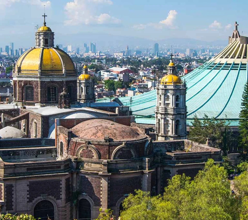 Catedral con c&uacute;pulas doradas, ciudad al fondo y cielo azul con nubes.