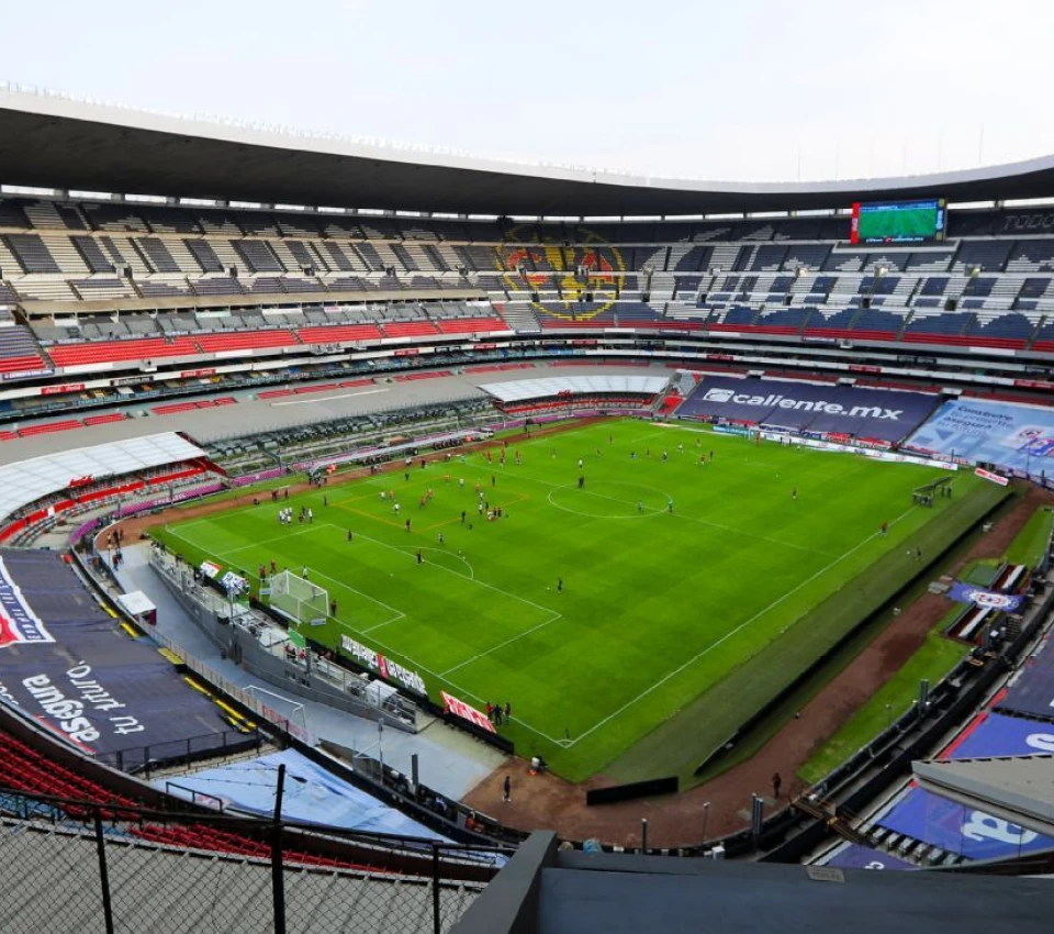 Estadio de f&uacute;tbol vac&iacute;o con jugadores entrenando en el campo.