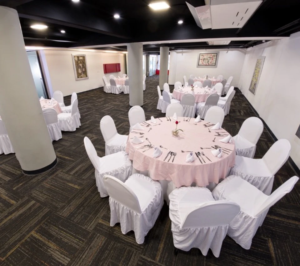 Sala de banquetes con mesas redondas y sillas con fundas blancas.