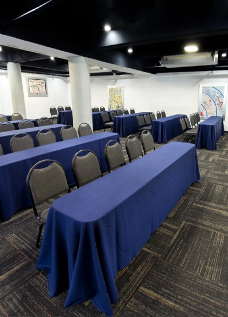 Sala de conferencias con mesas largas y sillas, lista para evento.