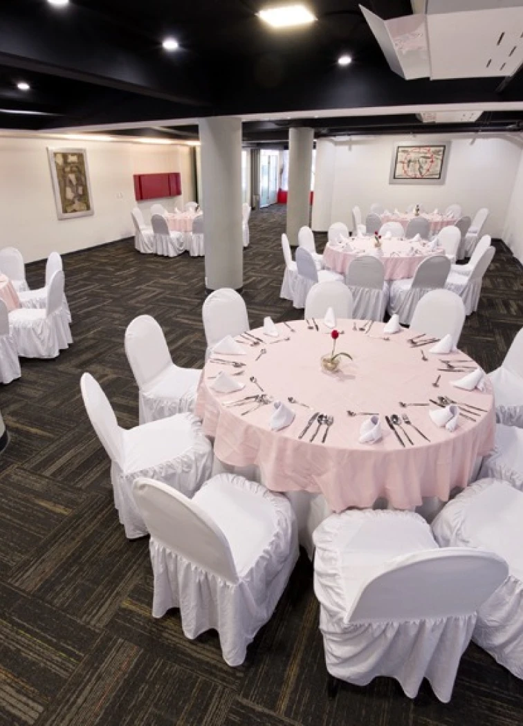 Sala de banquetes con mesas redondas y sillas blancas.