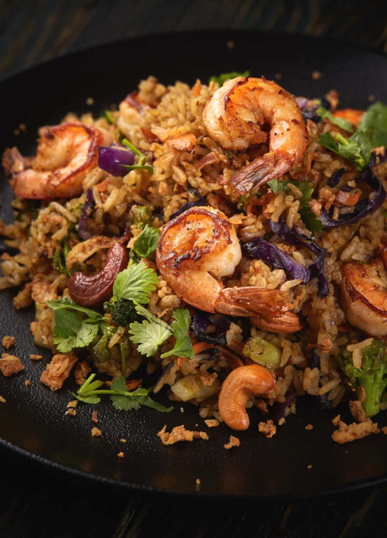 Arroz frito con camarones y verduras en plato negro.