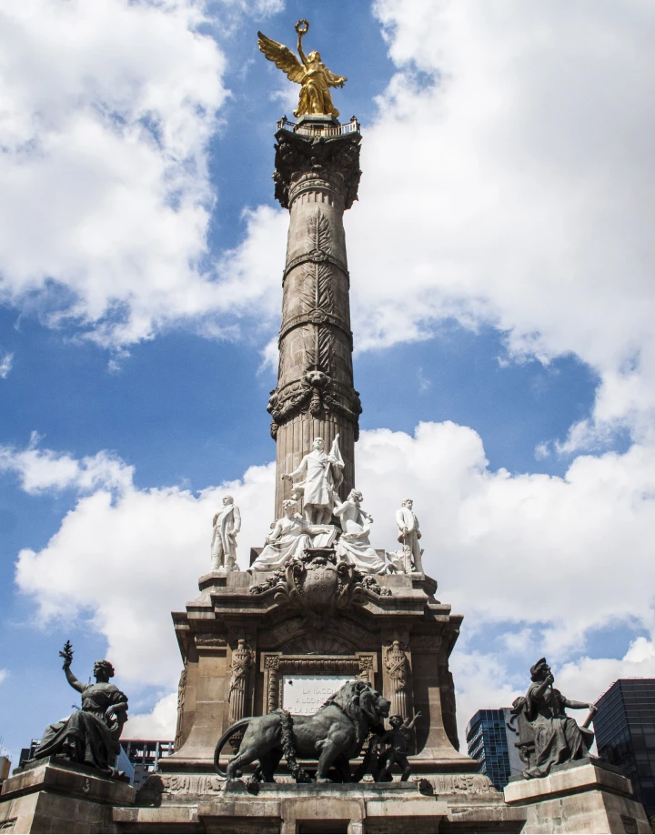 Monumento con una estatua dorada alada sobre una columna, cielo azul y nubes.