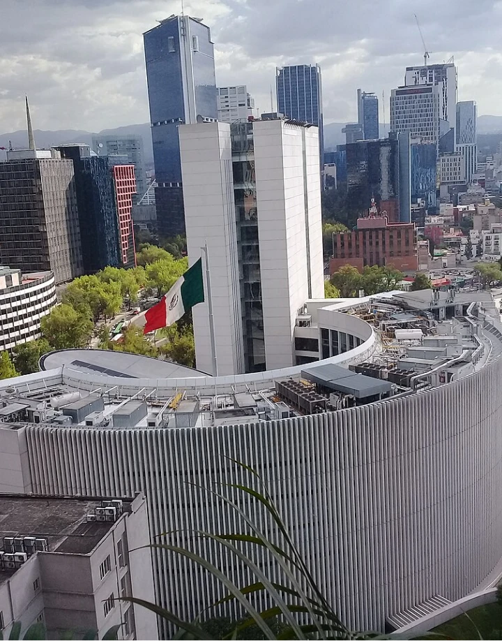 Edificio circular en ciudad con bandera de M&eacute;xico ondeando.