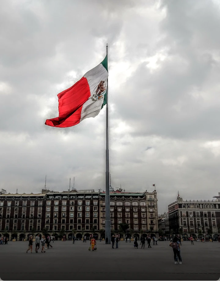 Bandera ondeando en el Z&oacute;calo de Ciudad de M&eacute;xico bajo un cielo nublado.