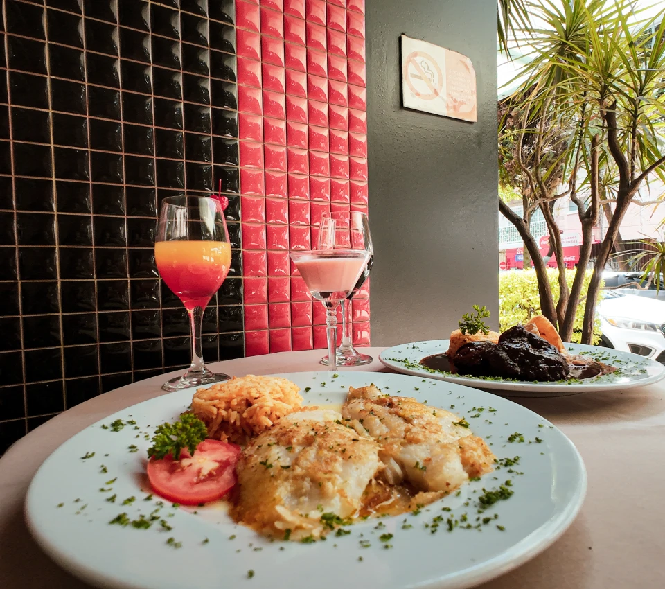 Platos de comida elegante con dos copas, en restaurante frente a jard&iacute;n.