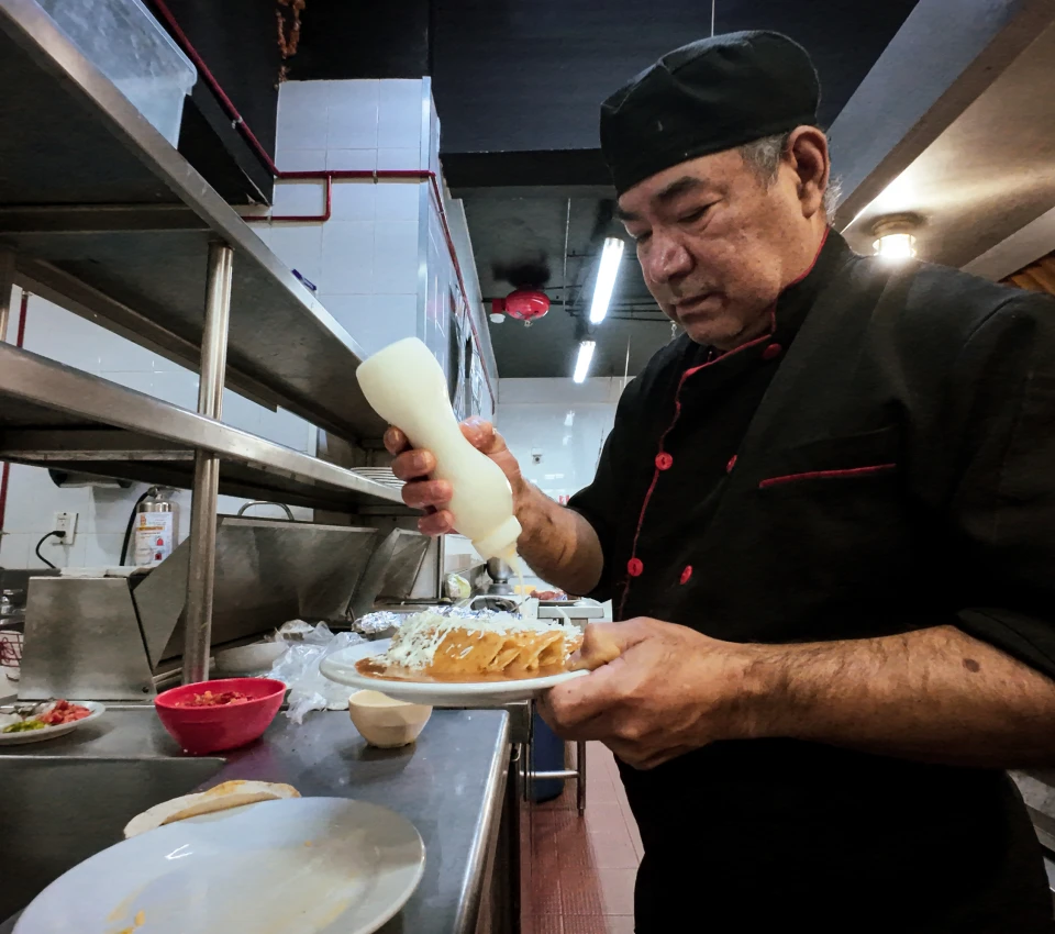 Chef decorando un platillo en la cocina con salsa blanca.
